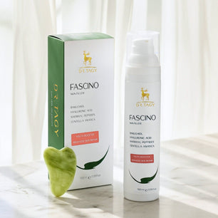 DR TAGY Fascino Skin Filler bottle displayed with its packaging on a marble surface, with a small green heart-shaped leaf in front and soft curtains in the background.